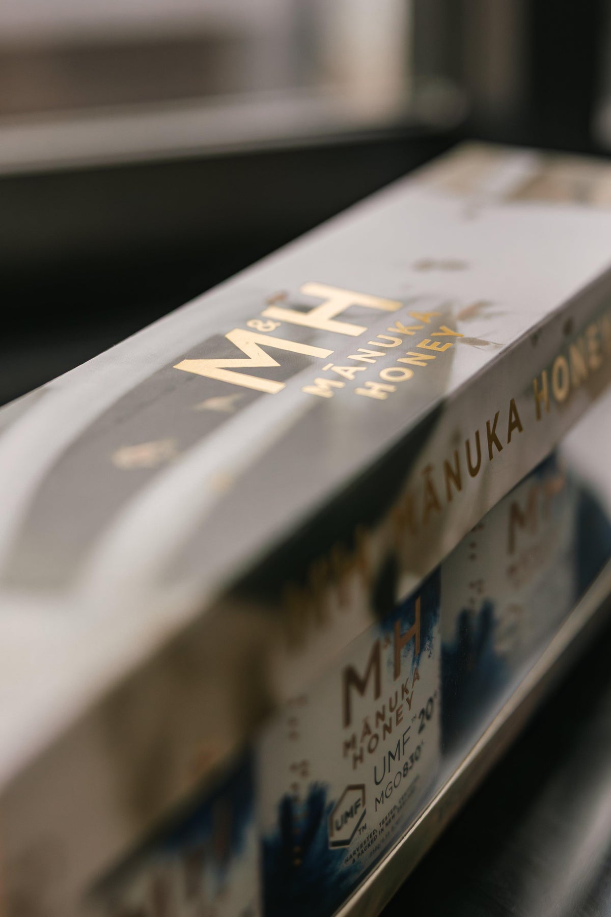 Manuka Honey packaging with 'M&H' branding on a reflective surface