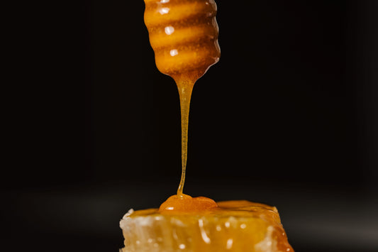 Manuka Honey, dripping down from a stirring spoon onto some honeycomb