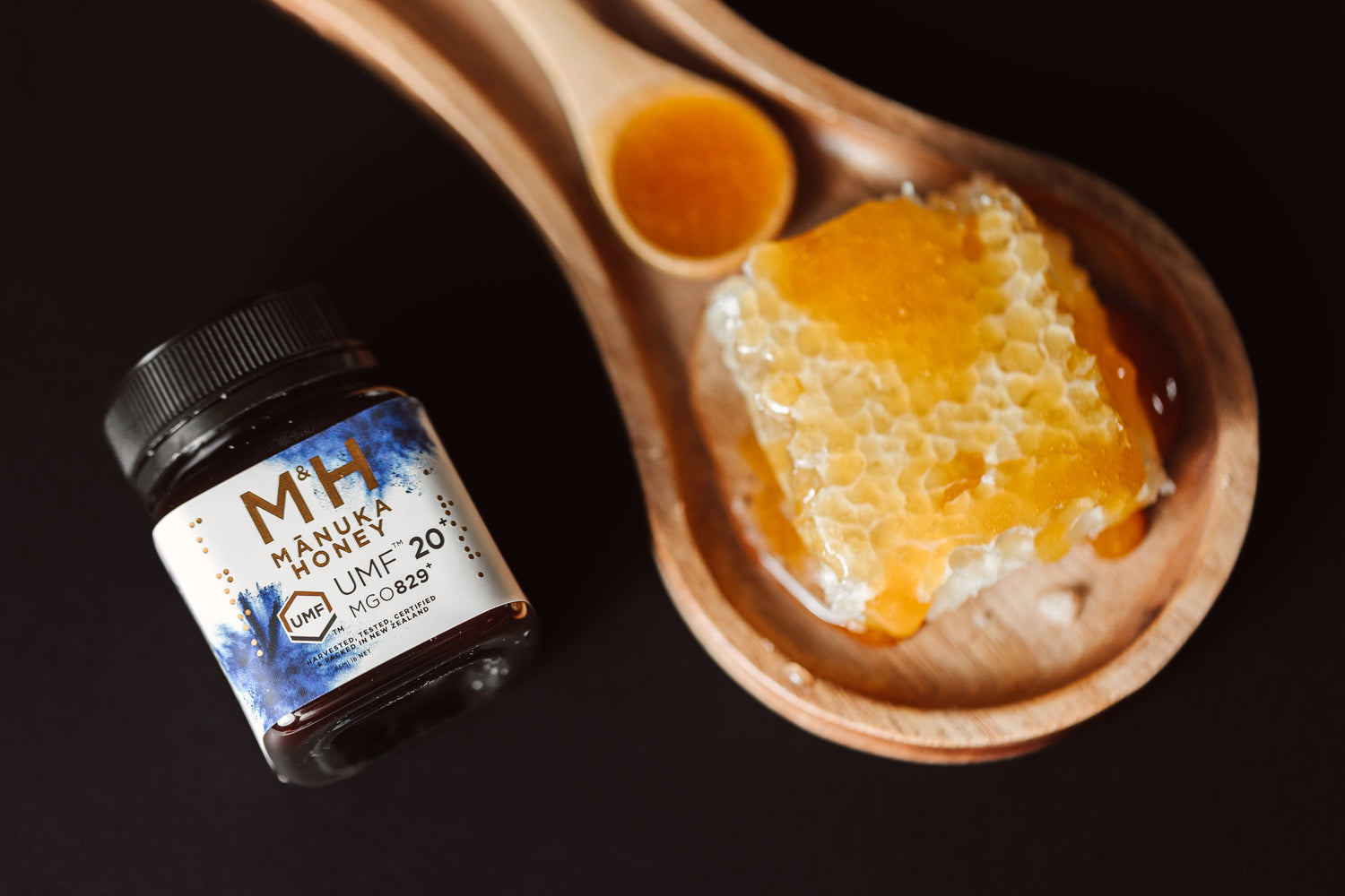 Manuka honey jar with a honeycomb and honey on a wooden spoon against a dark background